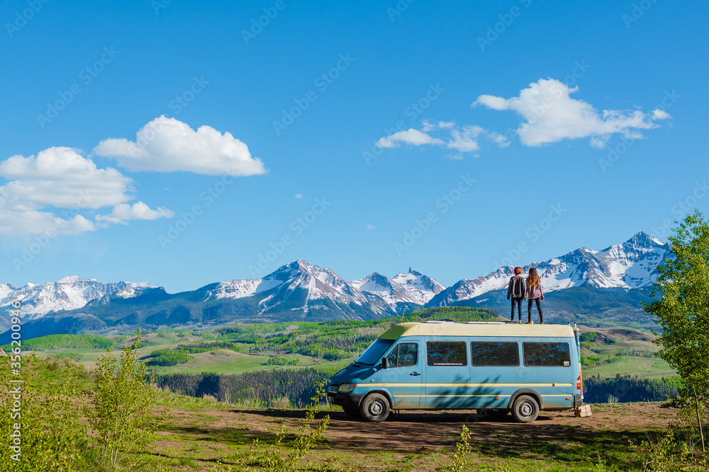couple standing on top of a camper van in front of mountain range couple standing on top of a camper van in front of mountain range