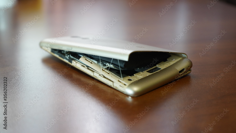 Swollen smartphone battery. Damaged smartphone with a faulty battery. Damaged phone on a wooden background. Swollen smartphone battery. Damaged smartphone with a faulty battery. Damaged phone on a wooden background.
