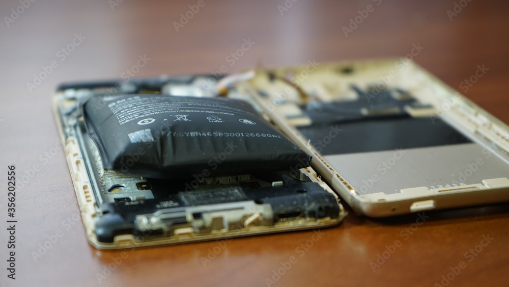 Swollen smartphone battery. Damaged smartphone with a faulty battery. Damaged phone on a wooden background. Swollen smartphone battery. Damaged smartphone with a faulty battery. Damaged phone on a wooden background.