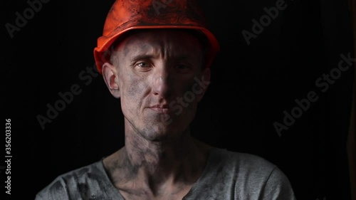 The face of a male miner in a helmet on a black background. Portrait of a tired mining worker. photo