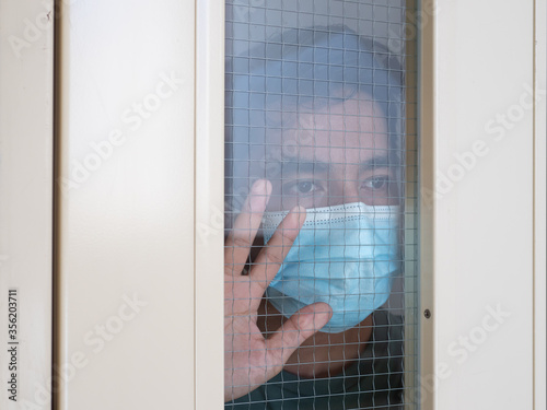 Lonely man in medical mask looking through the window. Isolation at home for self quarantine. Concept home quarantine, prevention COVID-19. Coronavirus outbreak situation