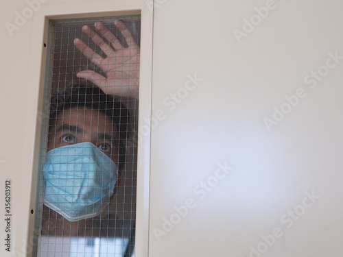 Lonely man in medical mask looking through the window. Isolation at home for self quarantine. Concept home quarantine, prevention COVID-19. Coronavirus outbreak situation