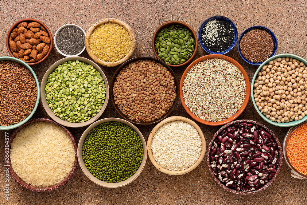 Assorted of a varied of legumes, beans, grains and seeds in bowls on a brown stone background. Top view, flat lay
