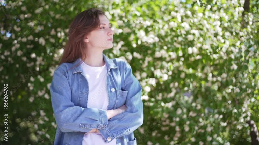 Woman portrait in flowers. A beautiful woman in denim stands against the background of jasmine flowers on the street Woman portrait in flowers. A beautiful woman in denim stands against the background of jasmine flowers on the street