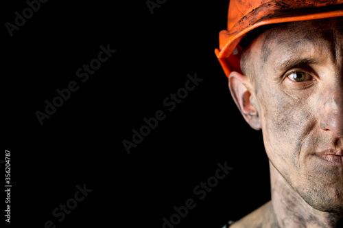 The face of a male miner in a helmet on a black background. Copy space.