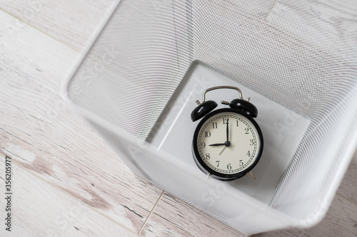 Top view of an alarm clock discarded in a white mesh metal trash bin. The concept of wasted time.