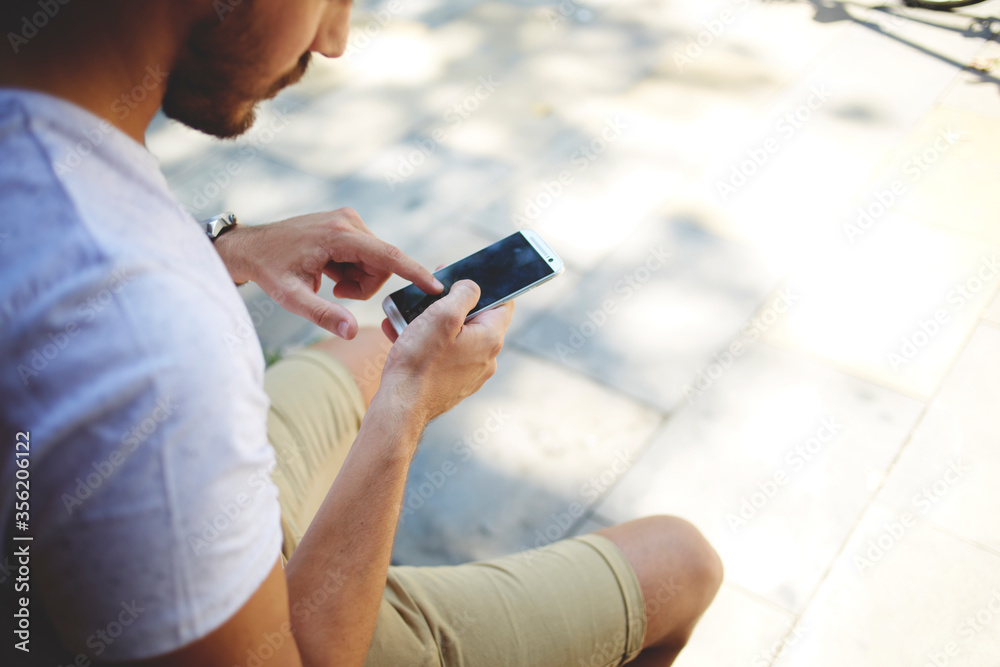 Hipster guy searching information on cell telephone while sitting outdoors
