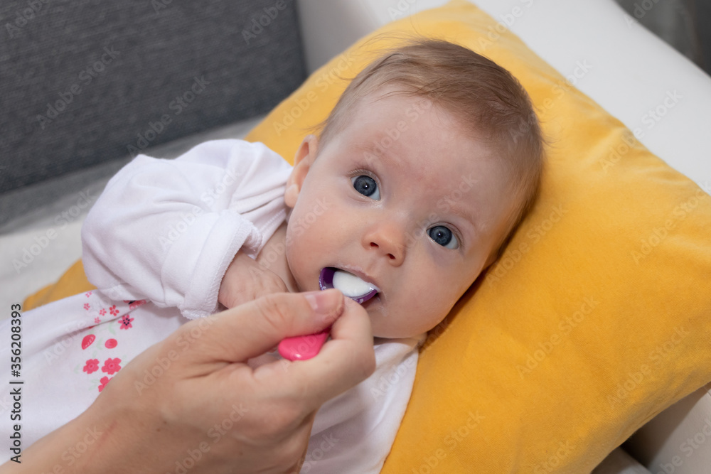 Mother feeding her baby girl with spoon. Happy little cute daughter with blue eyes. The baby girl is four months old. Mother feeding her baby girl with spoon. Happy little cute daughter with blue eyes. The baby girl is four months old.