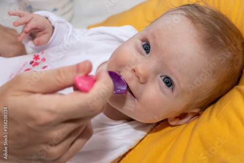 Mother feeding her baby girl with spoon. Happy little cute daughter with blue eyes. The baby girl is four months old.