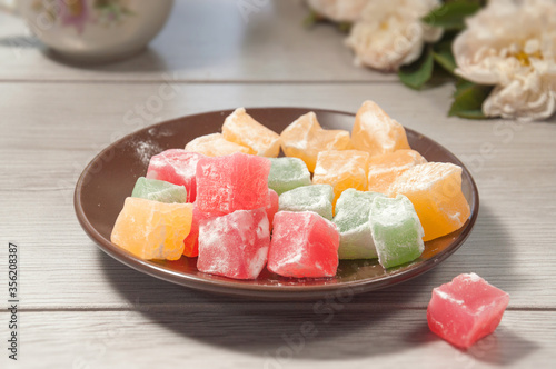 Colorful cubes of turkish delight in a ceramic plate on a wooden table. Traditional turkish sweets.