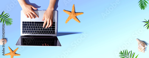 Person using a laptop computer with summer theme objects - flat lay