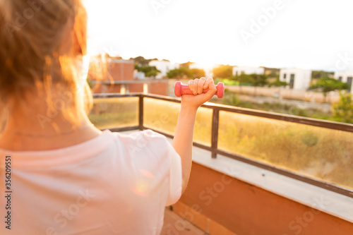 Chica rubia levantando una pesa al atardecer haciendo una actividad física en la terraza de su casa photo