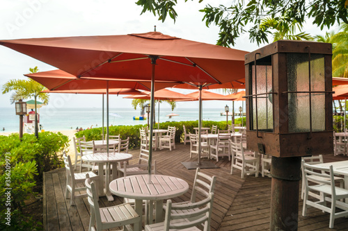Montego Bay, Jamaica. Restaurant terrace on the beach with large orange patio umbrellas and empty tables and chairs. Ocean in background. © Debbie Ann Powell