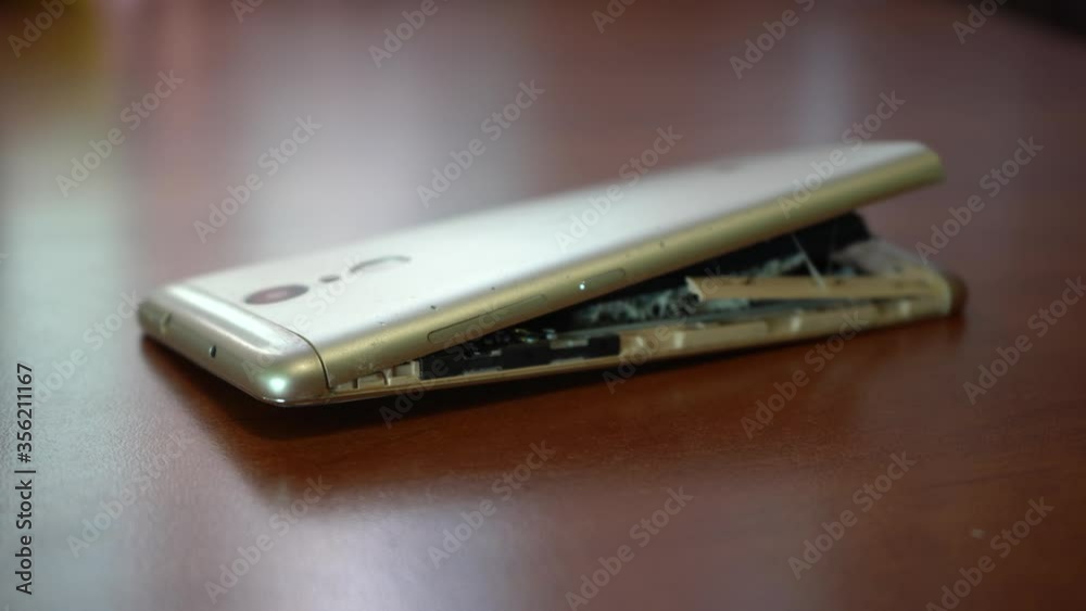 Swollen smartphone battery. Damaged smartphone with a faulty battery. Damaged phone on a wooden background. Swollen smartphone battery. Damaged smartphone with a faulty battery. Damaged phone on a wooden background.