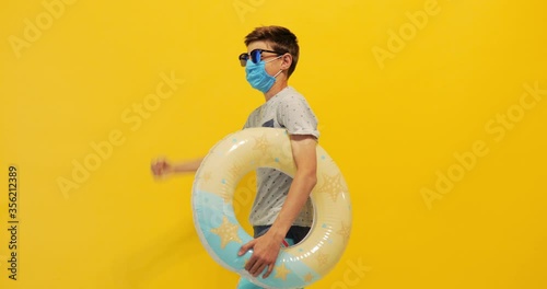  teen guy walks around with an inflatable ring and a medical protective mask on his face, on an isolated yellow background photo