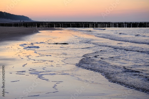 Beautiful sunset colors on the beach of sea and amazing reflection in water. Silhouette of breakwater on horizon.