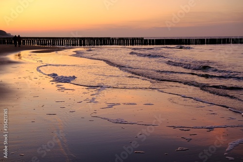 Fototapeta Naklejka Na Ścianę i Meble -  Beautiful sunset colors on the beach of sea and amazing reflection in water. Silhouette of breakwater on horizon.
