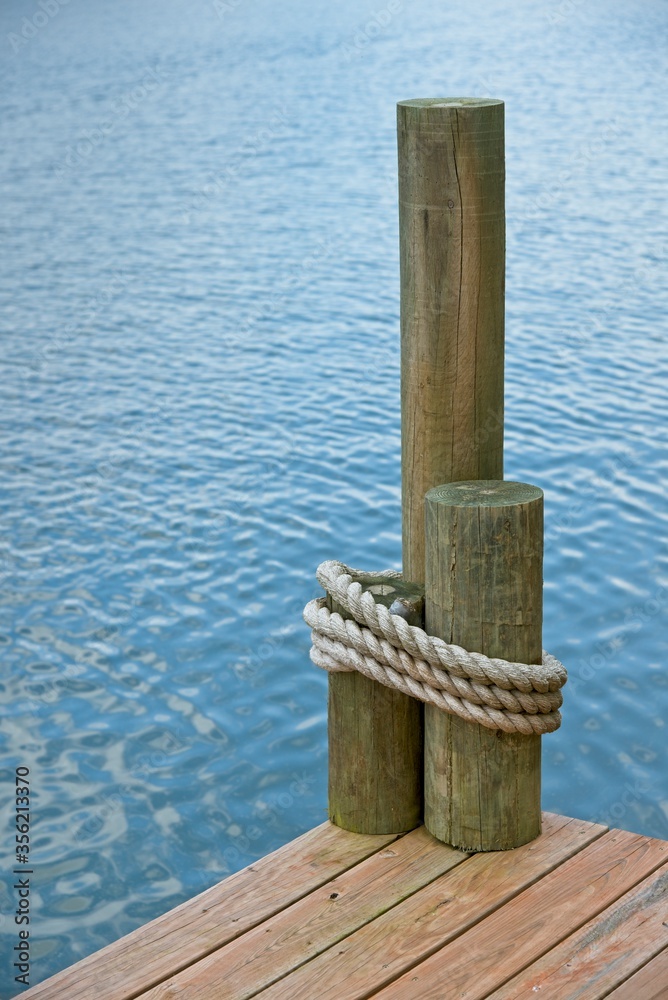 Naklejka premium The corner of a boat dock, on a lake, with rope wrapped around pilings.