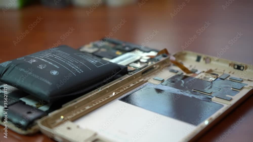 Swollen smartphone battery. Damaged smartphone with a faulty battery. Damaged phone on a wooden background. Swollen smartphone battery. Damaged smartphone with a faulty battery. Damaged phone on a wooden background.