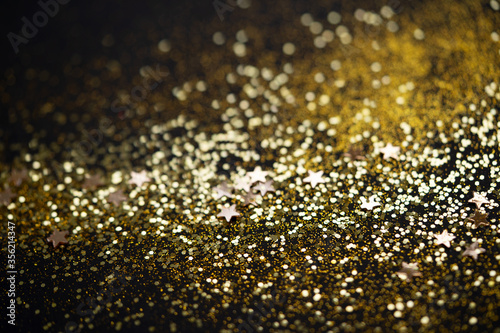 Beautiful Christmas light background. Abstract glitter bokeh and scattered sparkles in gold color, on black
