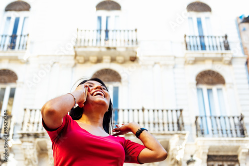 Latin woman smiling while talking on the phone and gesturing with her arms.