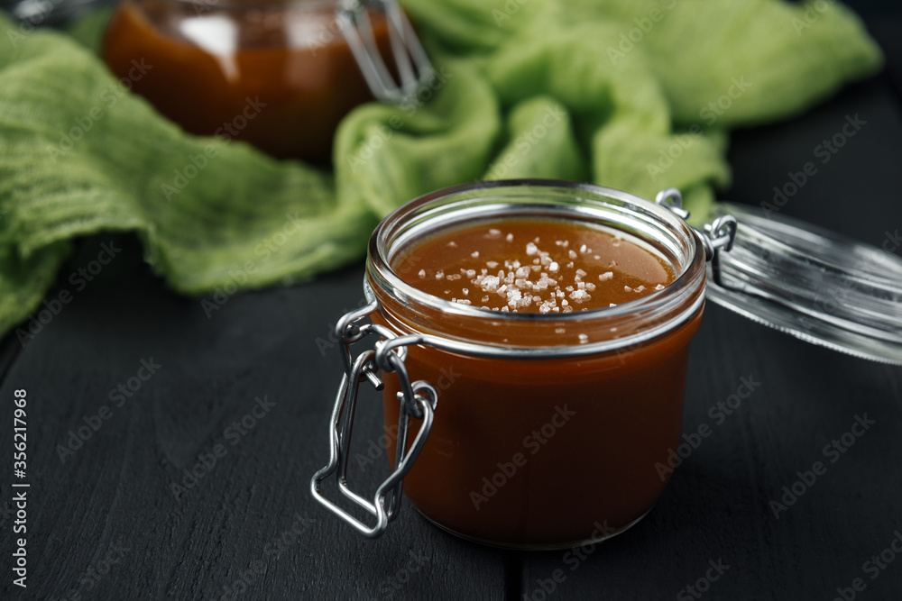 Two glass jars of homemade caramel with salt crystals on green gauze Two glass jars of homemade caramel with salt crystals on green gauze