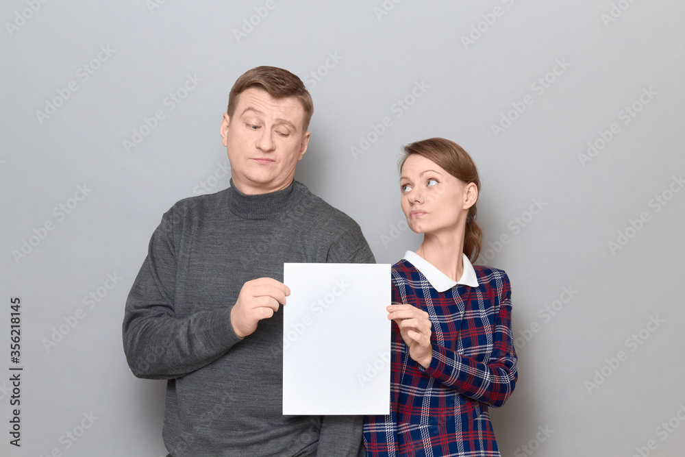 Portrait of adult couple holding together white blank paper sheet Portrait of adult couple holding together white blank paper sheet