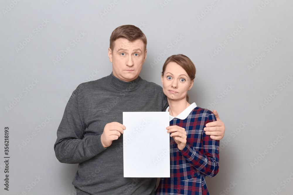 Portrait of adult couple holding together white blank paper sheet Portrait of adult couple holding together white blank paper sheet