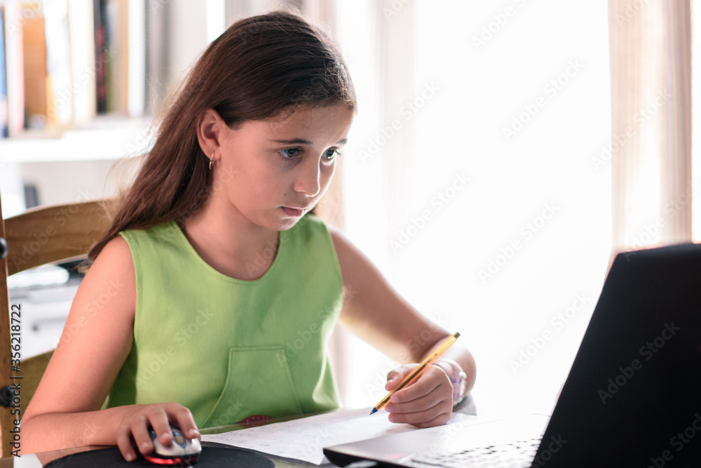 Little girl taking notes, doing homework at home in front of laptop. Education, learning and school concept. Little girl taking notes, doing homework at home in front of laptop. Education, learning and school concept.