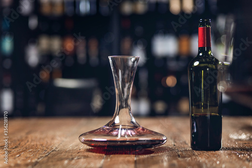 Red wine in bottle and decanter stands on wooden table in restaurant, dark background photo