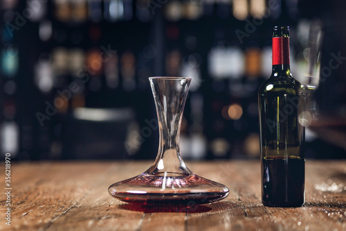 Foto Red wine in bottle and decanter stands on wooden table in restaurant, dark backg