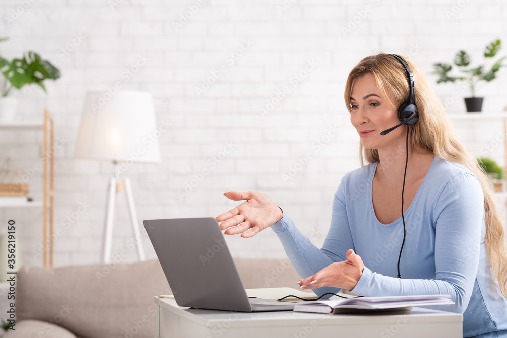 Communication with client from home. Woman with headphones and laptops sits at table Communication with client from home. Woman with headphones and laptops sits at table