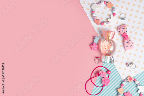 Children's flat lay. Perfume in the form of candy, children's jewelry and hair accessories on a pink background. Accessories for little girls