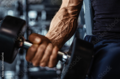 Hand holding dumbbell.Close up.Muscular arm in the gym.