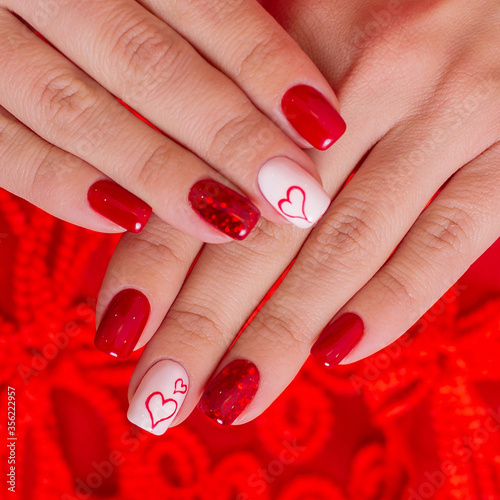 Female hands with beautiful fashion glamour manicure in red colours with heart design on nails