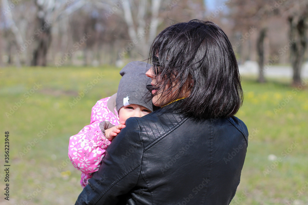 Dark-haired mother in glasses and a leather jacket holds her baby in her arms Dark-haired mother in glasses and a leather jacket holds her baby in her arms