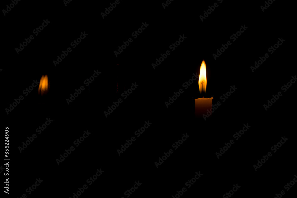 A lit candle in a dark room with reflection of the flame on glass