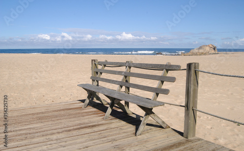 Banco de madeira num passadiço à entrada de uma praia com vista para o horizonte num dia quente de verão