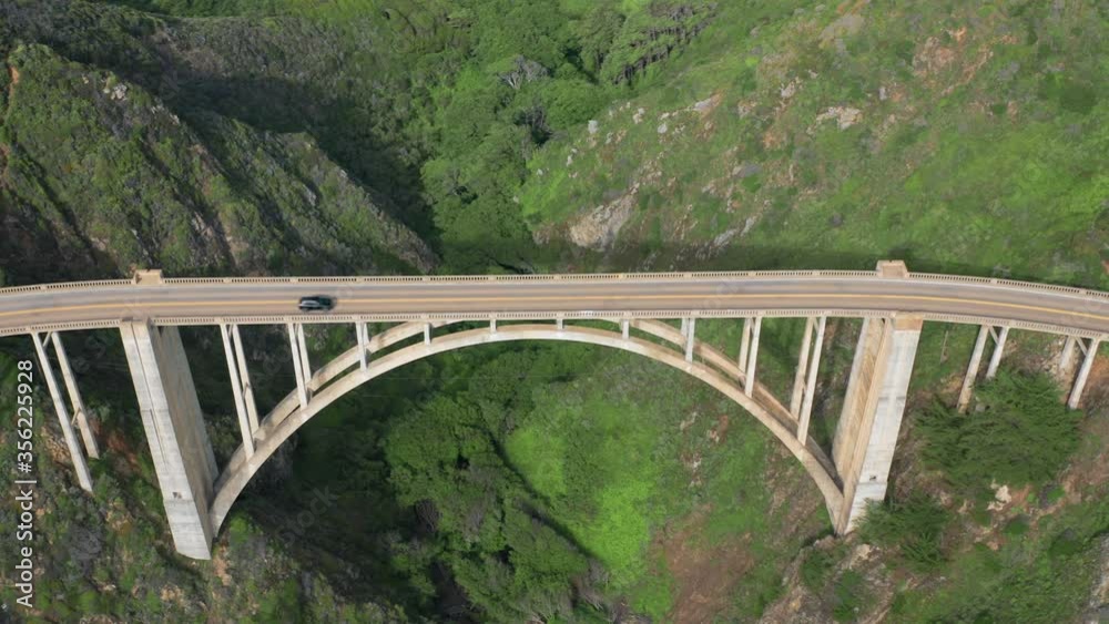 Aerial topdown survey over the high narrow concrete construction of Bixby Bridge crossing the creek on the coastline of Pacific Ocean and being a part of scenic coastal route. 4K Aerial topdown survey over the high narrow concrete construction of Bixby Bridge crossing the creek on the coastline of Pacific Ocean and being a part of scenic coastal route. 4K