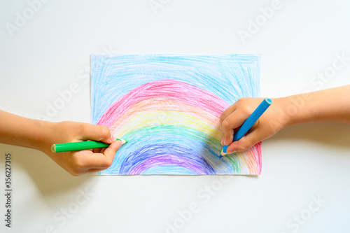 kid's hands together draw a rainbow colored pencils on white background photo