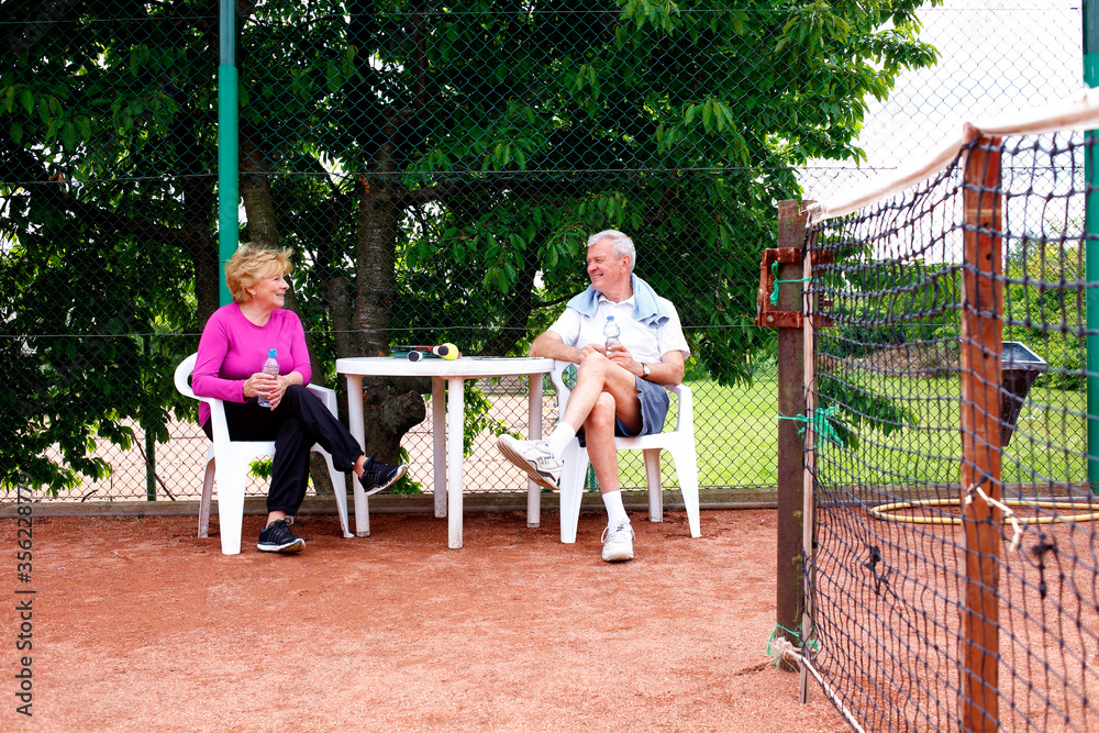 Happy senior couple relaxing at tennis court after playing tennis together