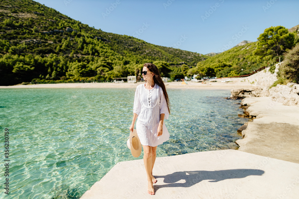 young woman in summer dress and hat relax on beach. Long hair woman travel on vacations to beach seaside.