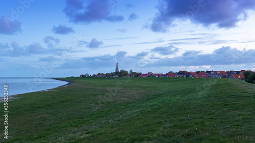Holland - Hindeloopen - a large coastal wall overgrown with grass, which protects the town from the tide. In the distance is a church with a white tower.