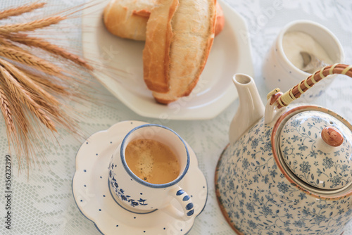 Close up of Breakfast served with french bread, tea cup, tea pot and sugar with wheat on white tablecloth