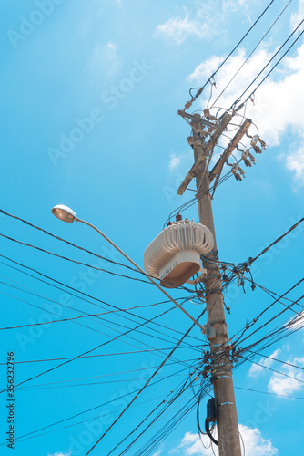 Concrete street lamp post with power transformer with tangle of electricity energy and communication wires with blue sky with clouds in the background