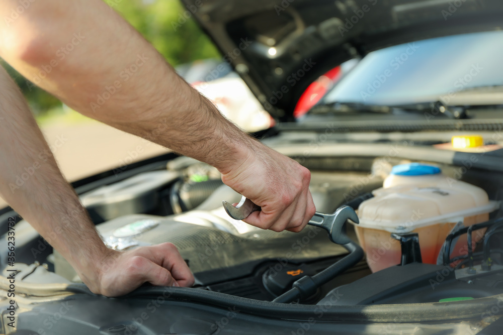 A man holds a wrench over a car engine. Car inspection A man holds a wrench over a car engine. Car inspection