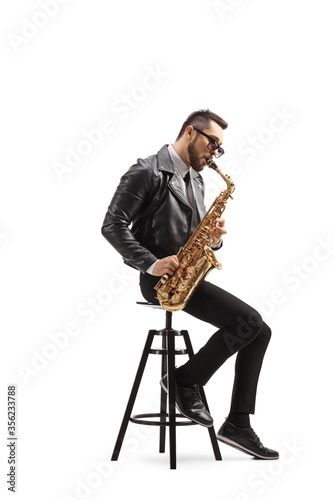 Man in a leather jacket sitting on a chair and playing a saxophone