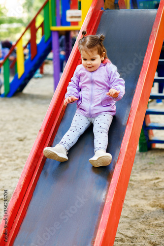 a little girl descends from a children's slide in the yard of her house, a colorful playground, a stylish child, the pleasure of playing, vertical photo © halcon1