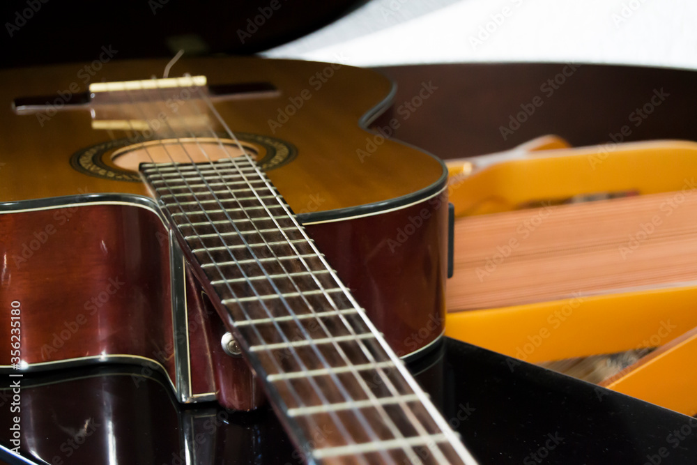 Fototapeta premium Acoustic Guitar lying down over the grand piano showing piano strings