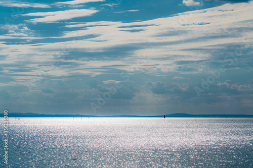 Blick über den Bodensee nach Westen mit gleißender Sonnenspiegellung uaf Seefläche, Segelbooten und dem Hohentwiel im Westen am Horizont photo